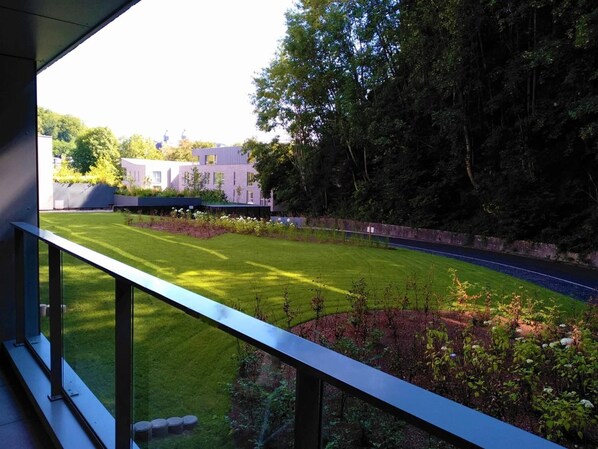 A view from a balcony overlooking a well-maintained lawn, a road, and a building with a modern design. - MY Hotel Malmedy (Malmedy)