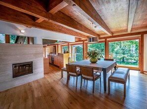 Een ruime keuken met houten balken, een eethoek met een tafel en stoelen, en grote ramen met uitzicht op de omgeving.
