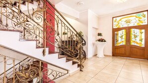 A grand staircase with ornate metal railings, a red accent wall, and a wooden door with floral glass panels. - Lesna Perla - Restaurant and Hotel (Rudziniec)