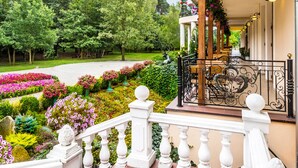 A covered outdoor area with a balcony, a garden with various plants and flowers, and a pathway leading to a building. - Lesna Perla - Restaurant and Hotel (Rudziniec)
