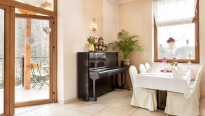 A dining area with a piano, a table set for four, and a view of the outdoors through a glass door. - Lesna Perla - Restaurant and Hotel (Rudziniec)