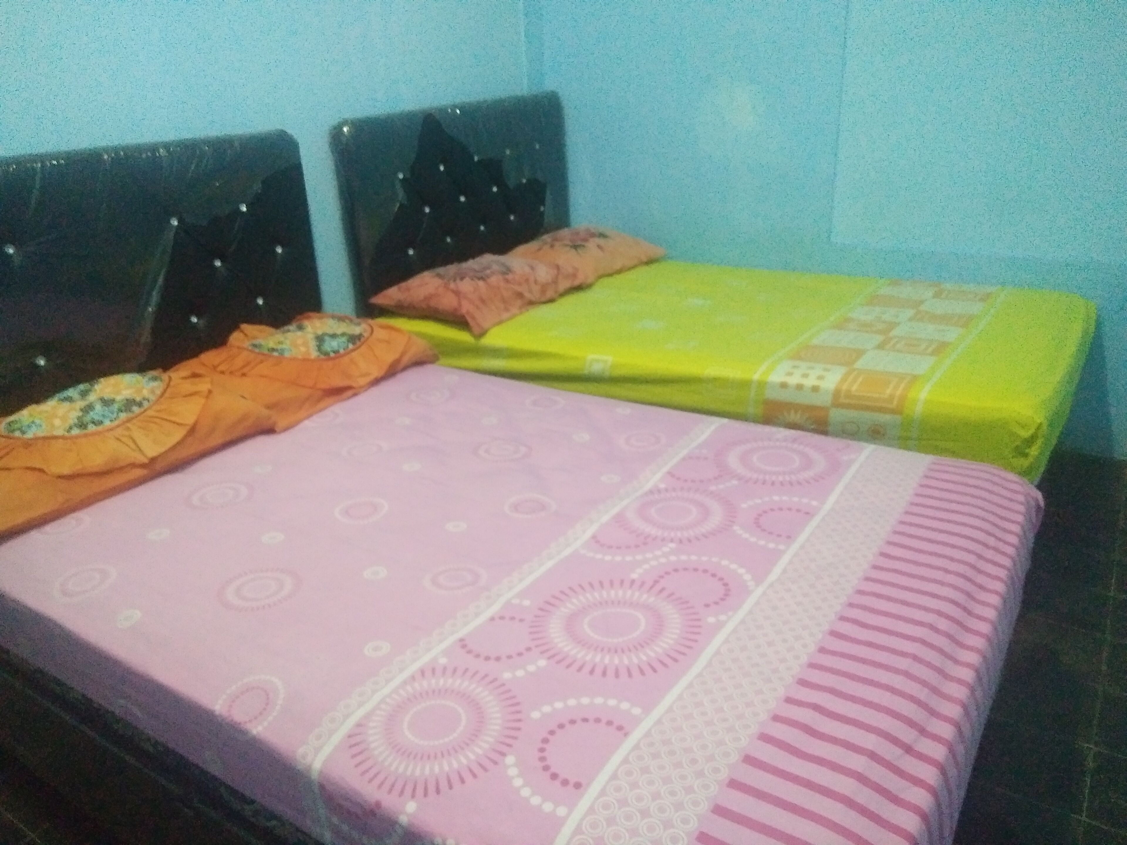 Una cama con colcha rosa y amarilla, dos almohadas y un cabecero.