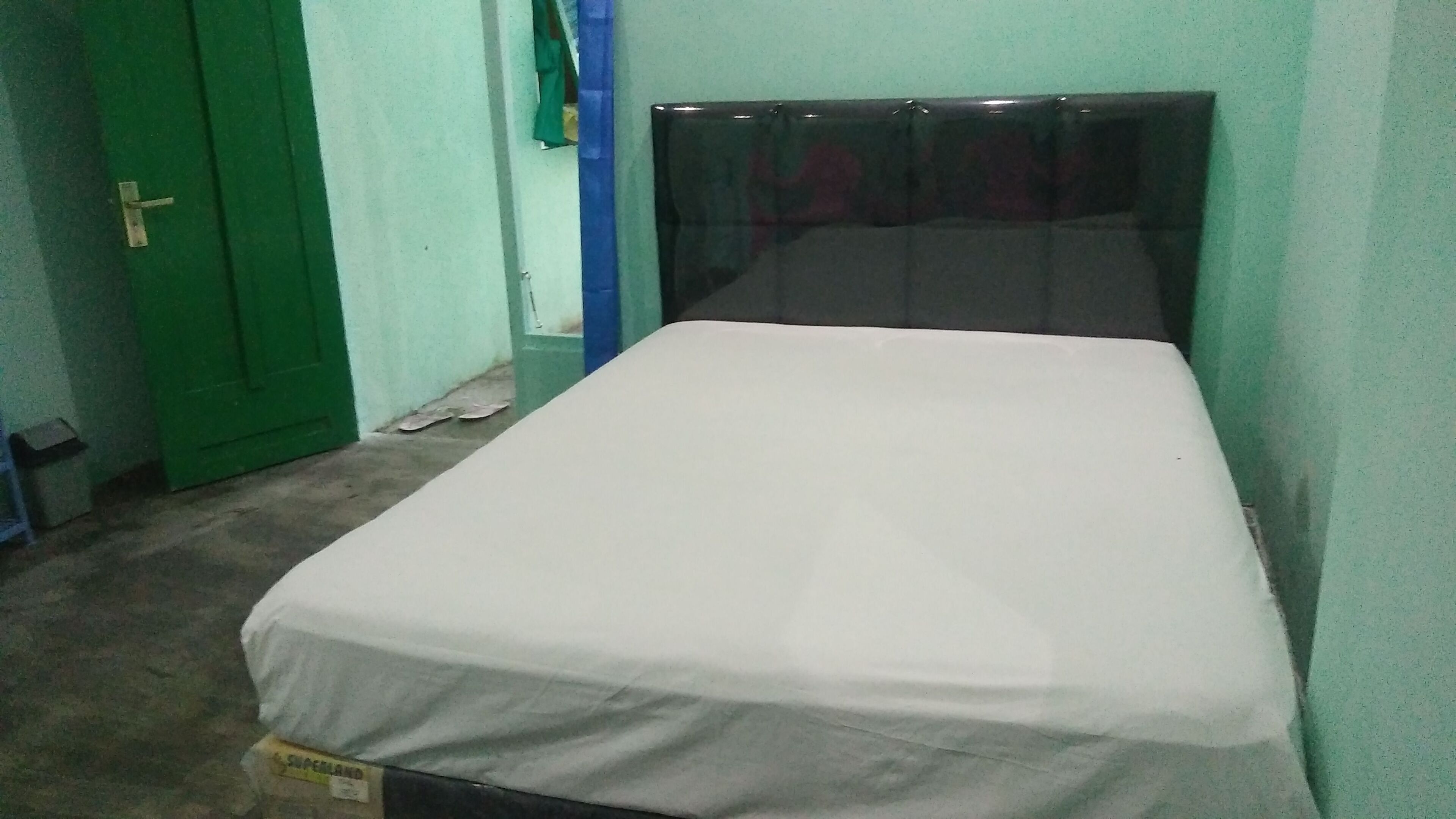 A small, single-bed room with a green door and a white mattress.