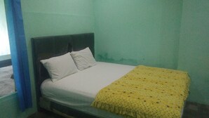 A single bed with a white mattress and pillows, a yellow blanket with floral patterns, and a dark headboard.