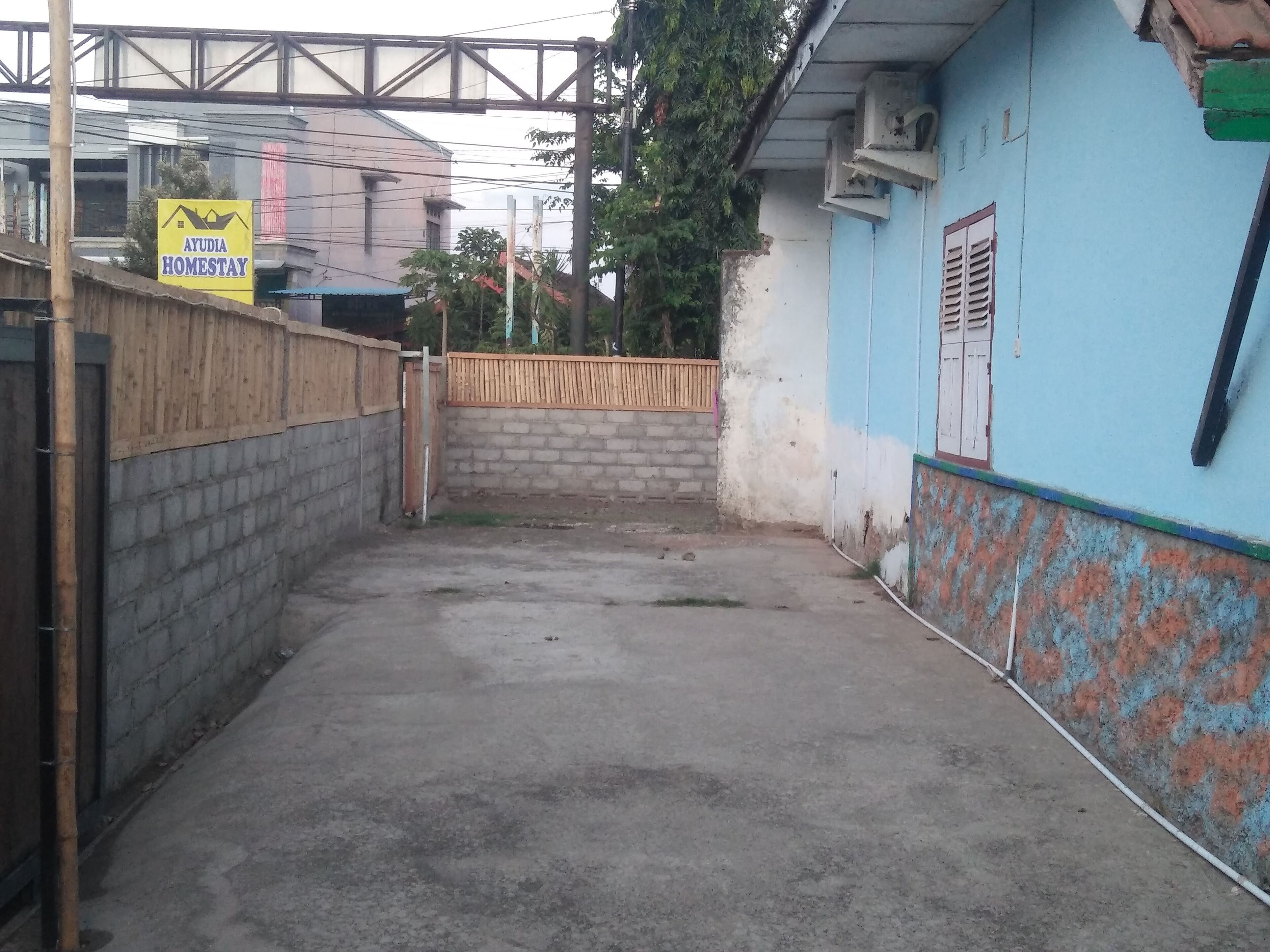 Un callejón estrecho con una verja de madera, un muro azul con una ventana y un cartel que indica Ayudia Homestay.