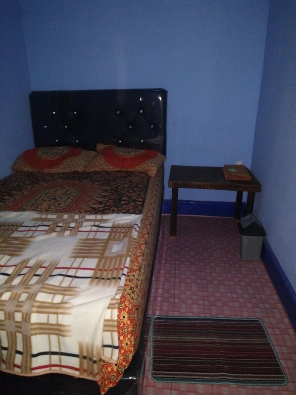 A bedroom with a bed, a bedside table, and a trash bin. - Ayudia Homestay (Banyuwangi)