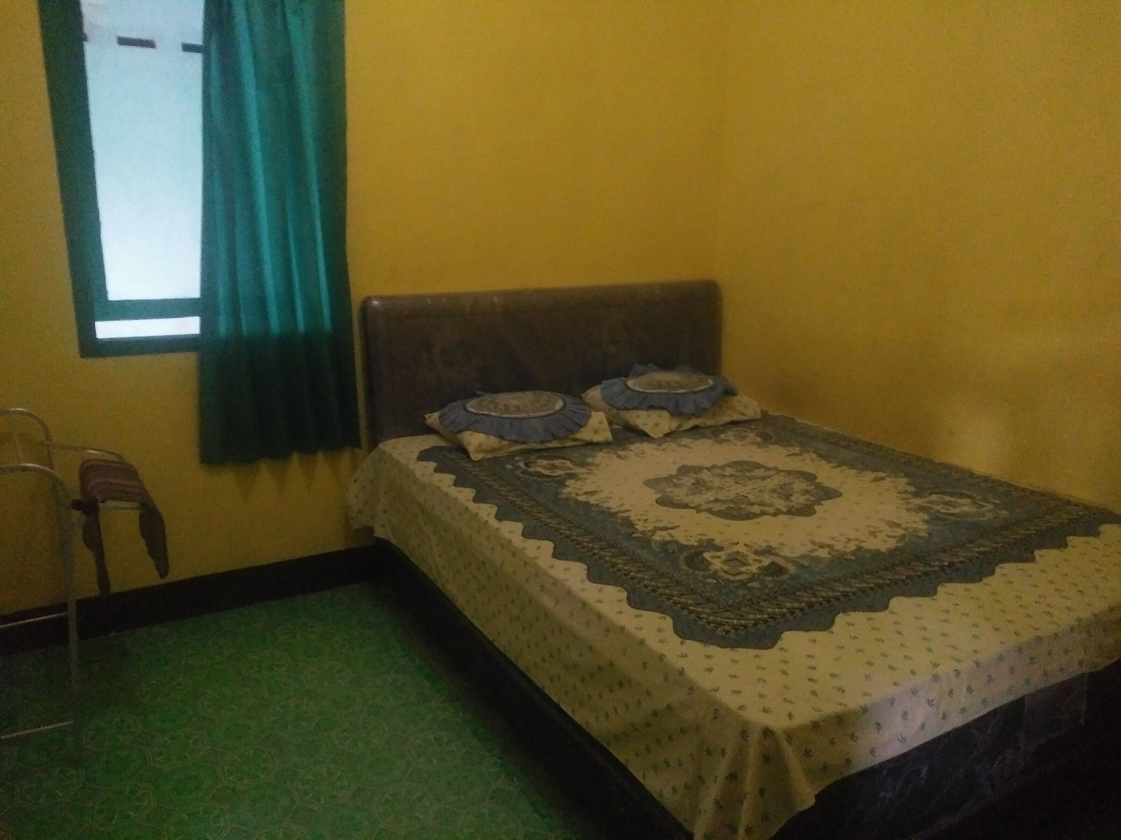 A small room with a bed, a window with curtains, a chair, and a green carpet.