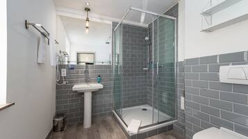 Un baño moderno con ducha de vidrio, lavabo pedestal y retrete.