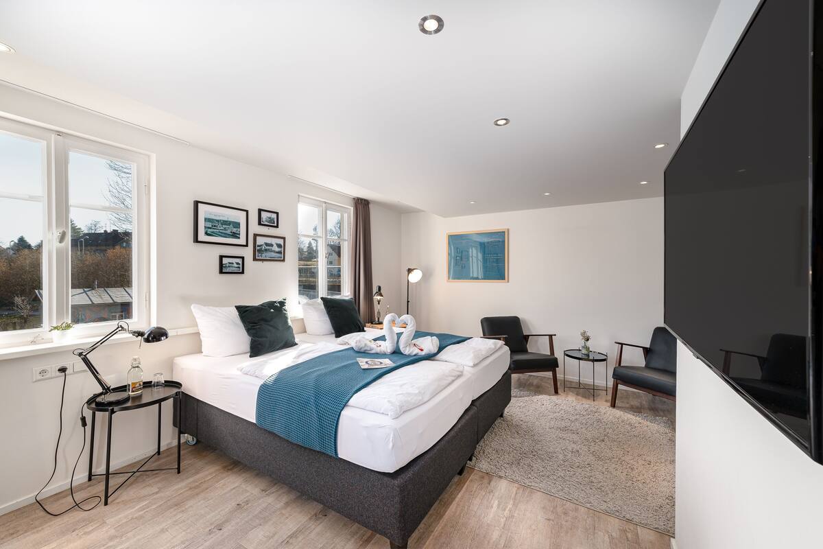 A modern bedroom with a large bed, a desk, a chair, and a TV.