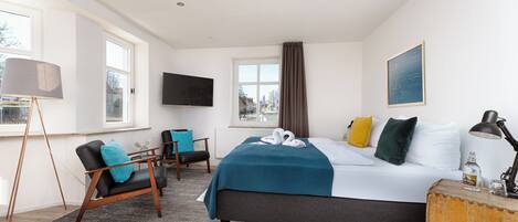 Quarto de hotel moderno com cama, escrivaninha, cadeira, televisão e janela com cortinas.