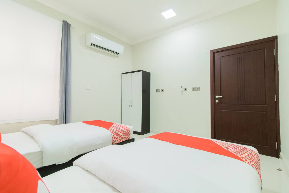 A hotel room with two beds, a wardrobe, an air conditioning unit, and a door.