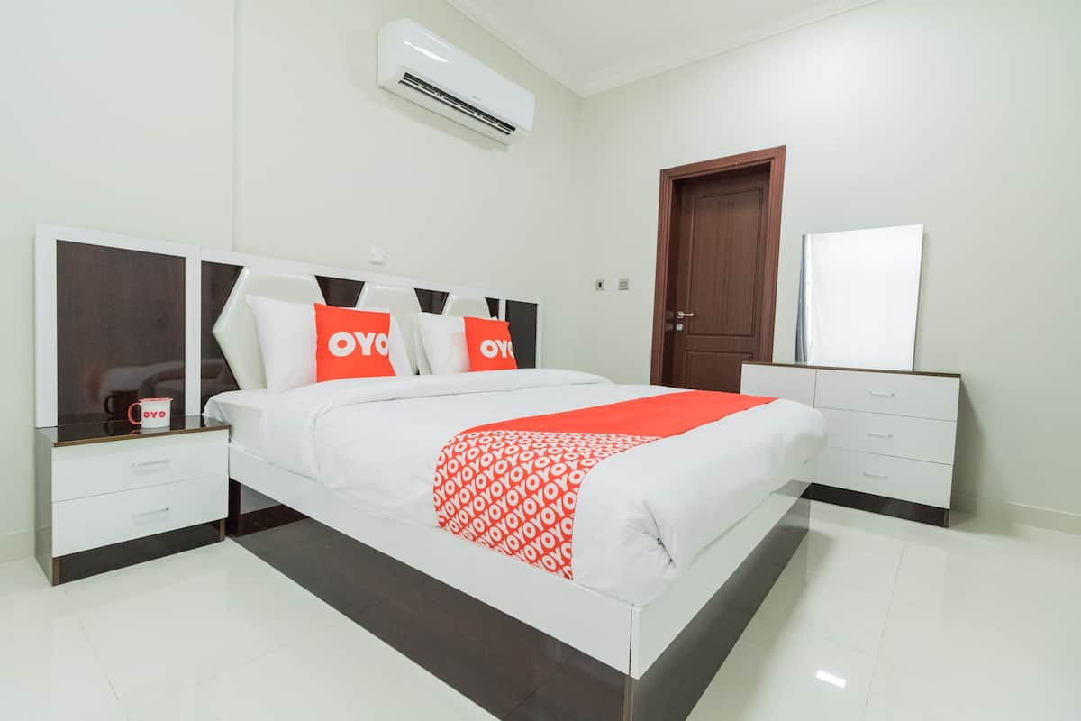 A modern bedroom with a white bed, orange pillows, a red blanket, and a white dresser.