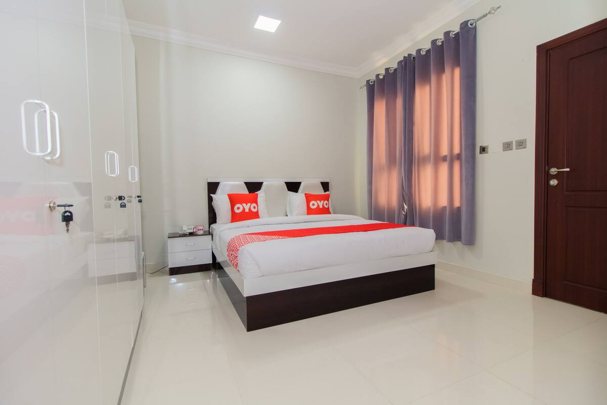A modern hotel room with a large bed, a nightstand, a wardrobe, and a door.