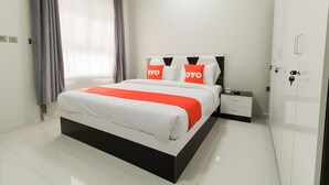A modern hotel room with a large bed, a nightstand, a wardrobe, and a window with curtains. - Super OYO 106 Muscat Grand Hotel Apartment (Seeb)