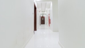 A clean, well-lit hallway with white walls and a shiny floor, leading to a door at the end. - Super OYO 106 Muscat Grand Hotel Apartment (Seeb)