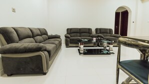 A living room with a sectional sofa, two armchairs, and a coffee table with decorative items. - Super OYO 106 Muscat Grand Hotel Apartment (Seeb)