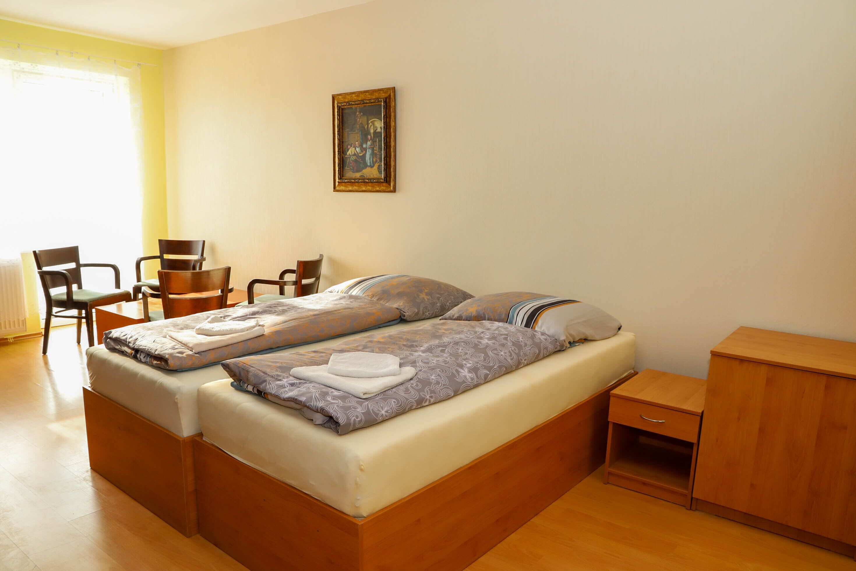 Ein Schlafzimmer mit einem Bett, zwei Stühlen, einer kleinen Kommode und einem Bild an der Wand.