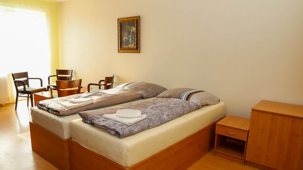 A bedroom with a bed, two chairs, a small cabinet, and a painting on the wall. - Hotel Zátoka (Senec)