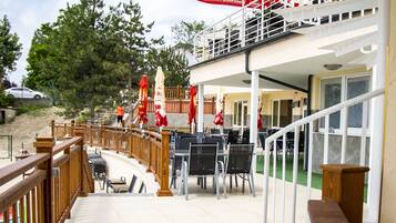 Un espacio al aire libre cubierto con mesas y sillas, una terraza de madera y sombrillas rojas.