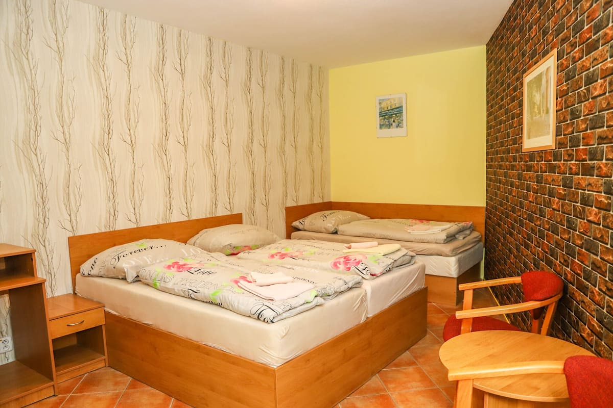 A bedroom with a wooden bed, a nightstand, a chair, and a brick-patterned wall.