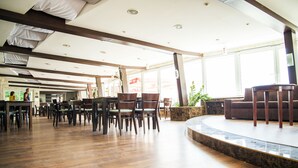 A spacious indoor area with wooden flooring, a curved seating area, and large windows allowing natural light. - Hotel Zátoka (Senec)