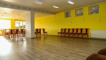 A spacious room with wooden flooring, yellow walls, and multiple wooden chairs arranged for seating.