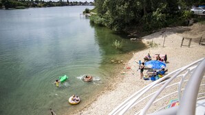 A lakeside view with clear water, a sandy beach, and people engaging in water activities. - Hotel Zátoka (Senec)