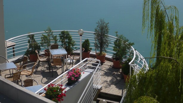 A balcony with outdoor furniture, potted plants, and a view of a body of water. - Hotel Zátoka (Senec)