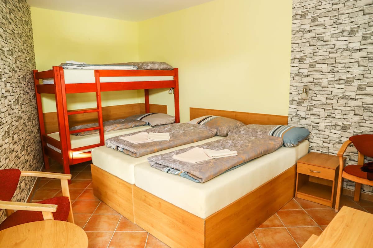 A bunk bed with two levels, a wooden nightstand, a chair, and a tiled floor.