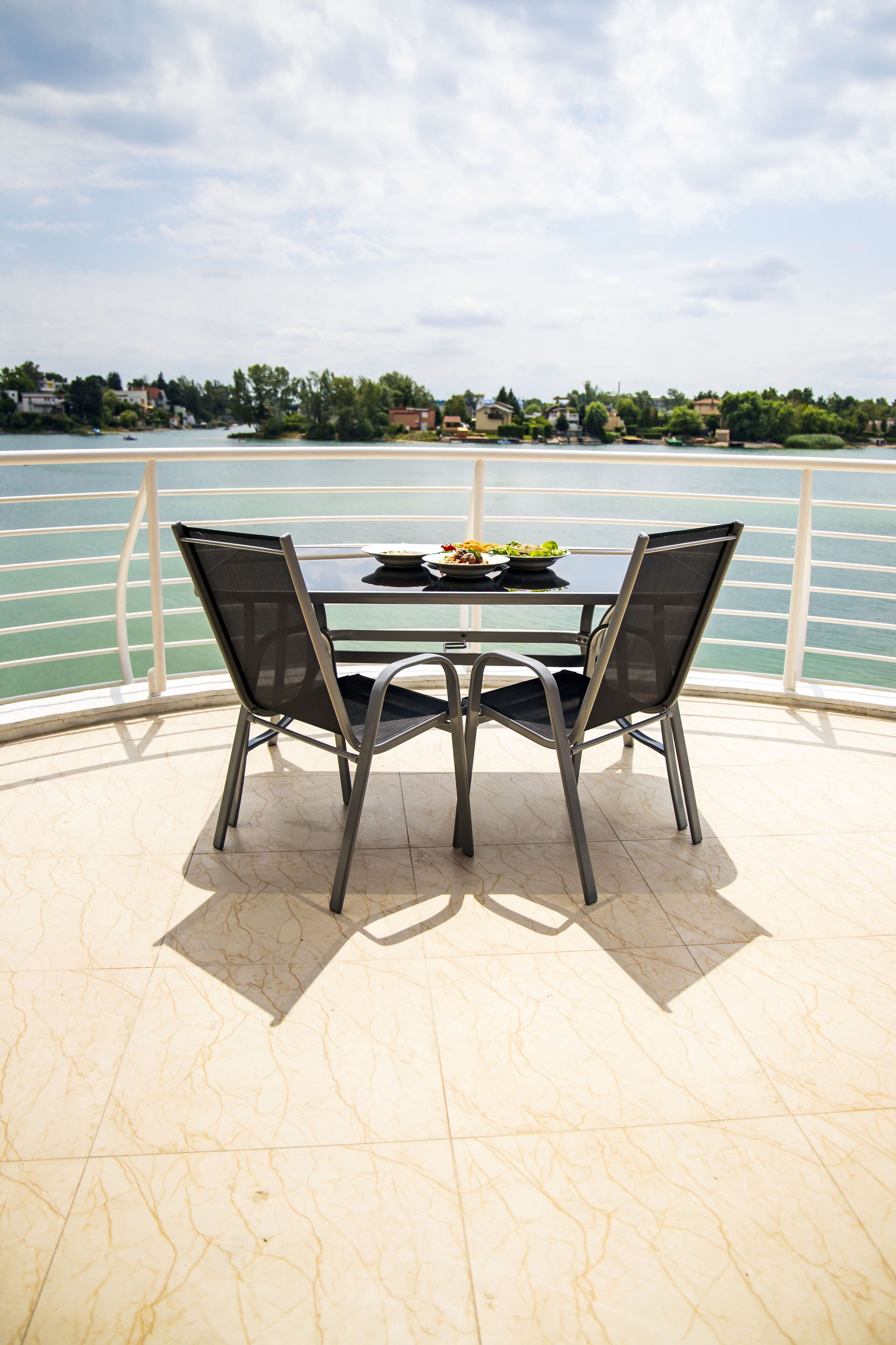 A table with two chairs on a balcony overlooking a body of water.