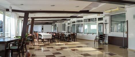 A spacious dining area with high ceilings, large windows, and a checkered floor.
