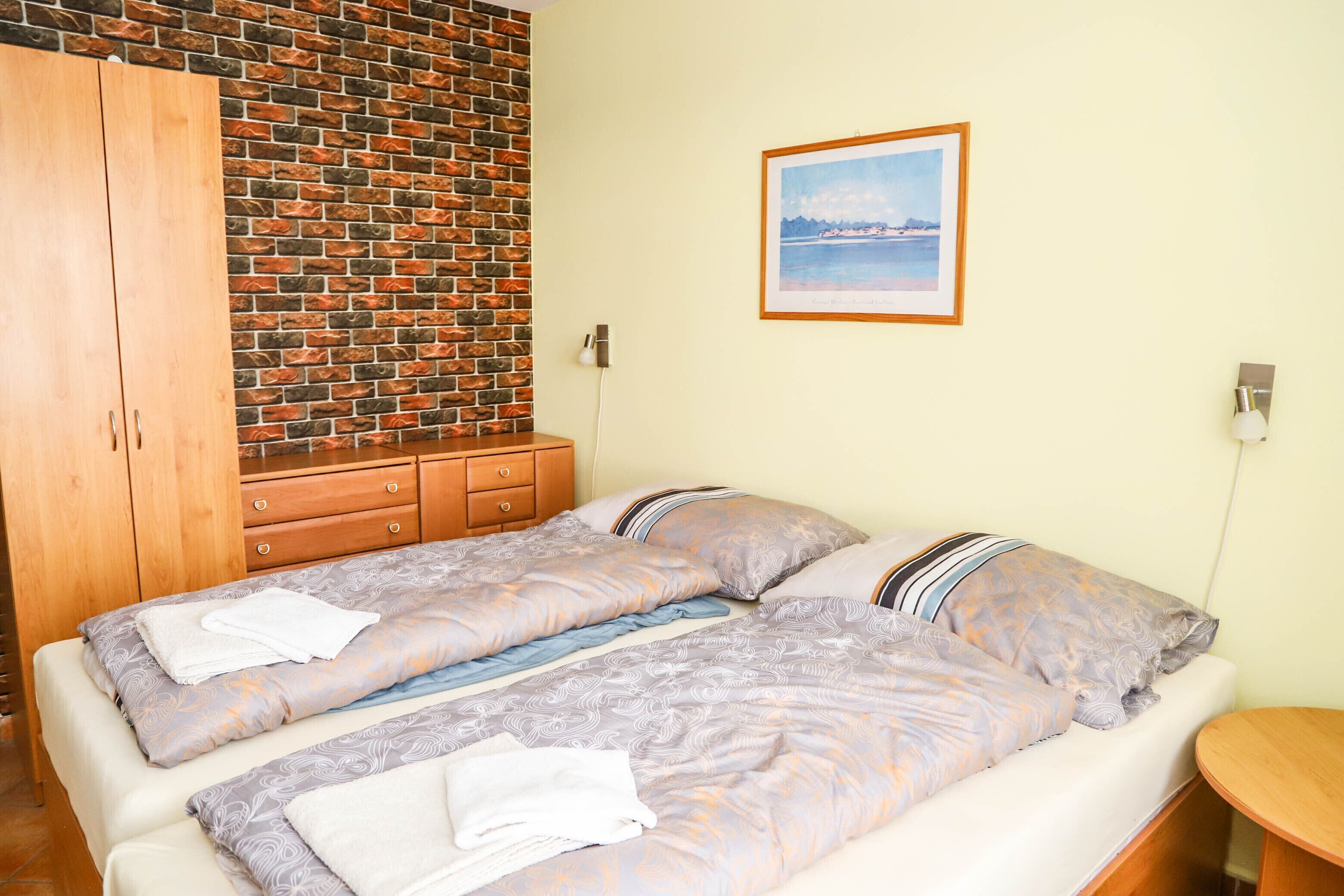 Una cama doble con ropa de cama estampada, un armario de madera, una pared de ladrillo y un cuadro enmarcado en la pared.