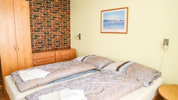 A double bed with patterned bedding, a wooden wardrobe, a brick wall, and a framed picture on the wall.