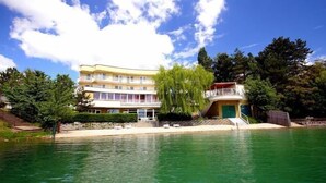 A large hotel with a pool, surrounded by trees and a clear sky. - Hotel Zátoka (Senec)