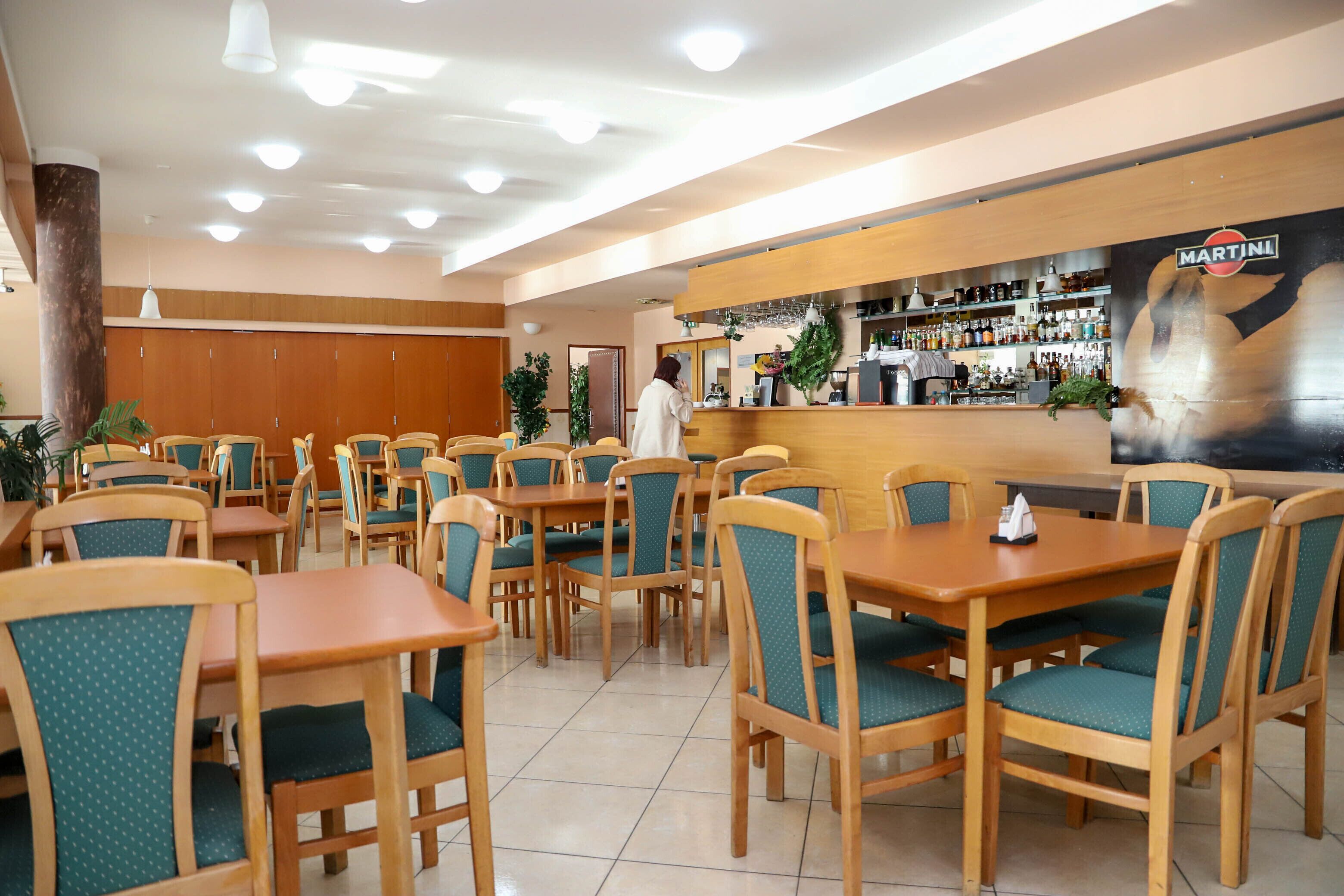 A restaurant with wooden tables and chairs, a bar area with a Martini sign, and a tiled floor.