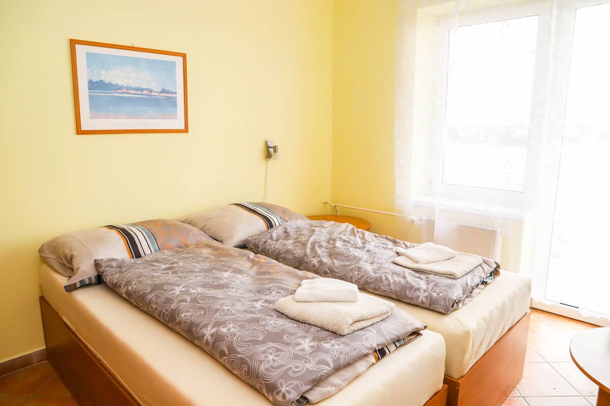 A double bed with patterned bedding, a framed picture on the wall, and a window with a view.