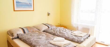 A double bed with patterned bedding, a framed picture on the wall, and a window with a view.