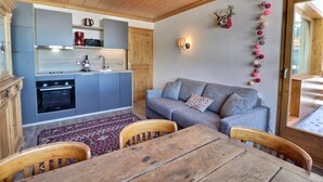 Eine kompakte Küche mit grauen Schränken, einer Holzbalkendecke und einem grauen Sofa mit gemusterten Kissen.