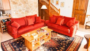 Un salon avec deux canapés rouges, une table basse en bois, un mur en pierre, un escalier en bois et une porte.