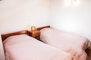 Une chambre avec deux lits simples, une table de chevet avec une lampe et une prise électrique au mur.