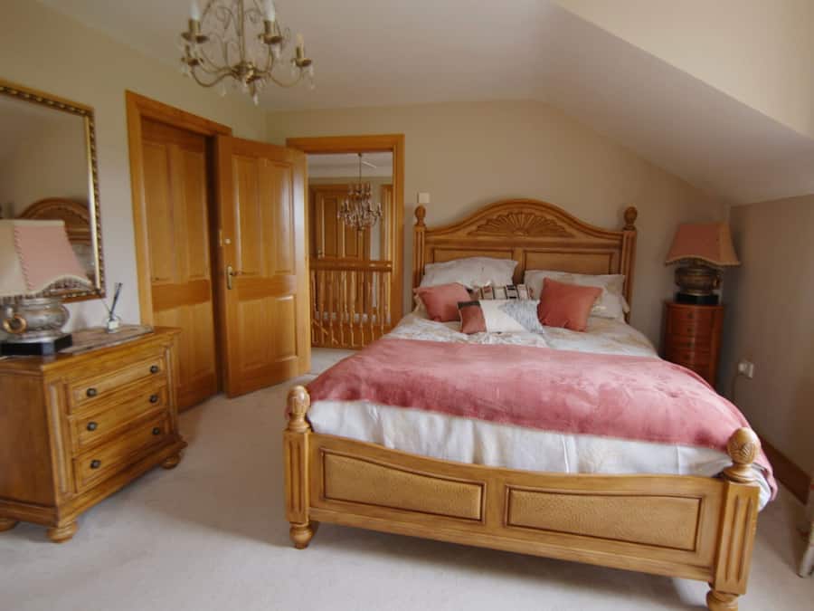 A bedroom with a wooden bed, a dresser, a mirror, and a chandelier.
