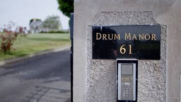 A black sign with gold lettering reading "DRUM MANOR 61" mounted on a stone wall, with a keypad below it.