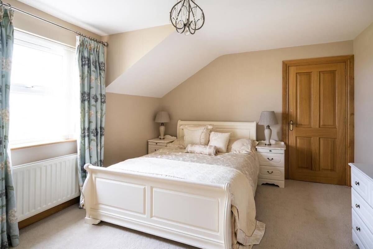 A bedroom with a large bed, a nightstand, a dresser, a wooden door, and a window with curtains.