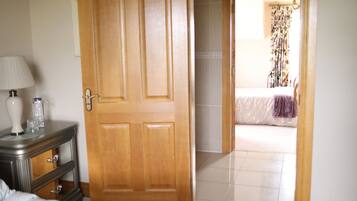 A bedroom with a bed, a dresser, a lamp, and a door leading to another room.
