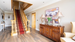 A spacious living area with a wooden staircase, a large painting, and a cream-colored sofa. - Drum Manor (Hillsborough)