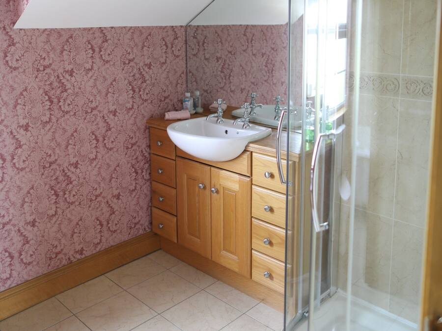 Un baño con tocador de madera, lavamanos blanco y ducha con cerramiento de vidrio.
