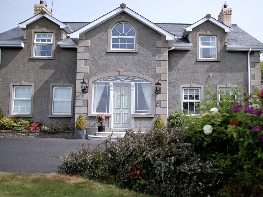 A two-story house with a symmetrical facade, a central entrance with a glass door, and a small porch with potted plants.