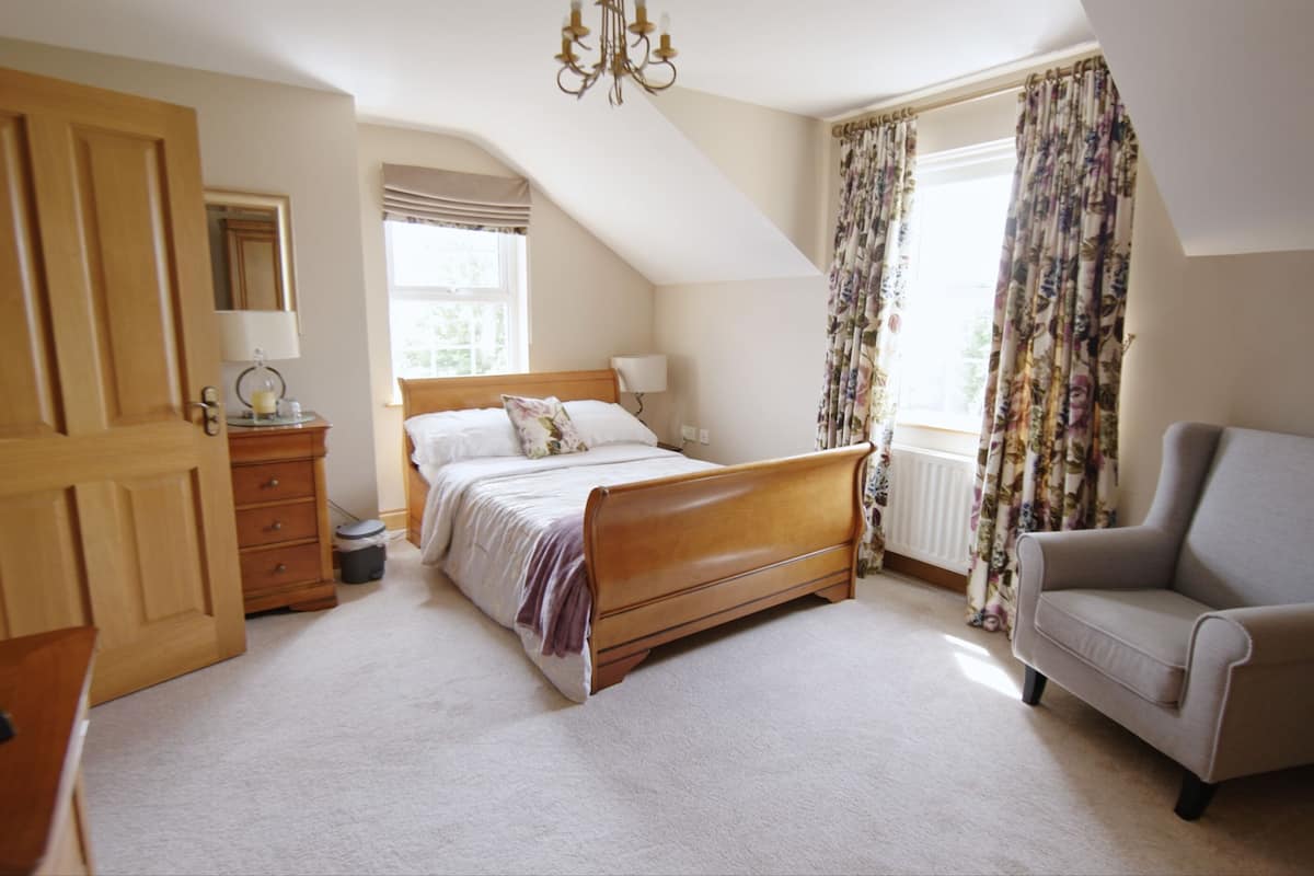 A bedroom with a wooden bed, a chair, a dresser, and a window with curtains.