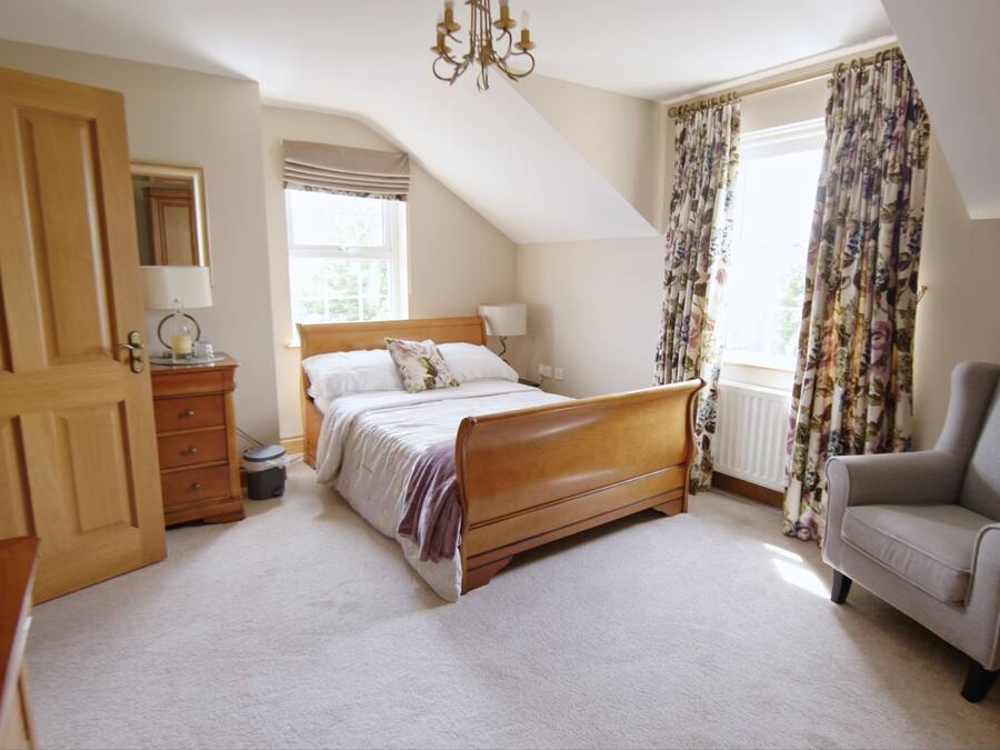 Une chambre à coucher avec un lit en bois, une chaise, une commode et une fenêtre avec des rideaux.