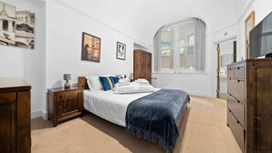 Una camera da letto con un letto grande, una cassettiera in legno, un comodino e una finestra con vista su un edificio.